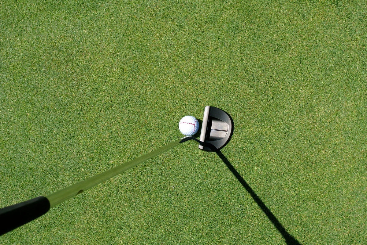 Putter und Golfball mit aufgezeichneter Ziellinie auf dem Grün, von oben fotografiert