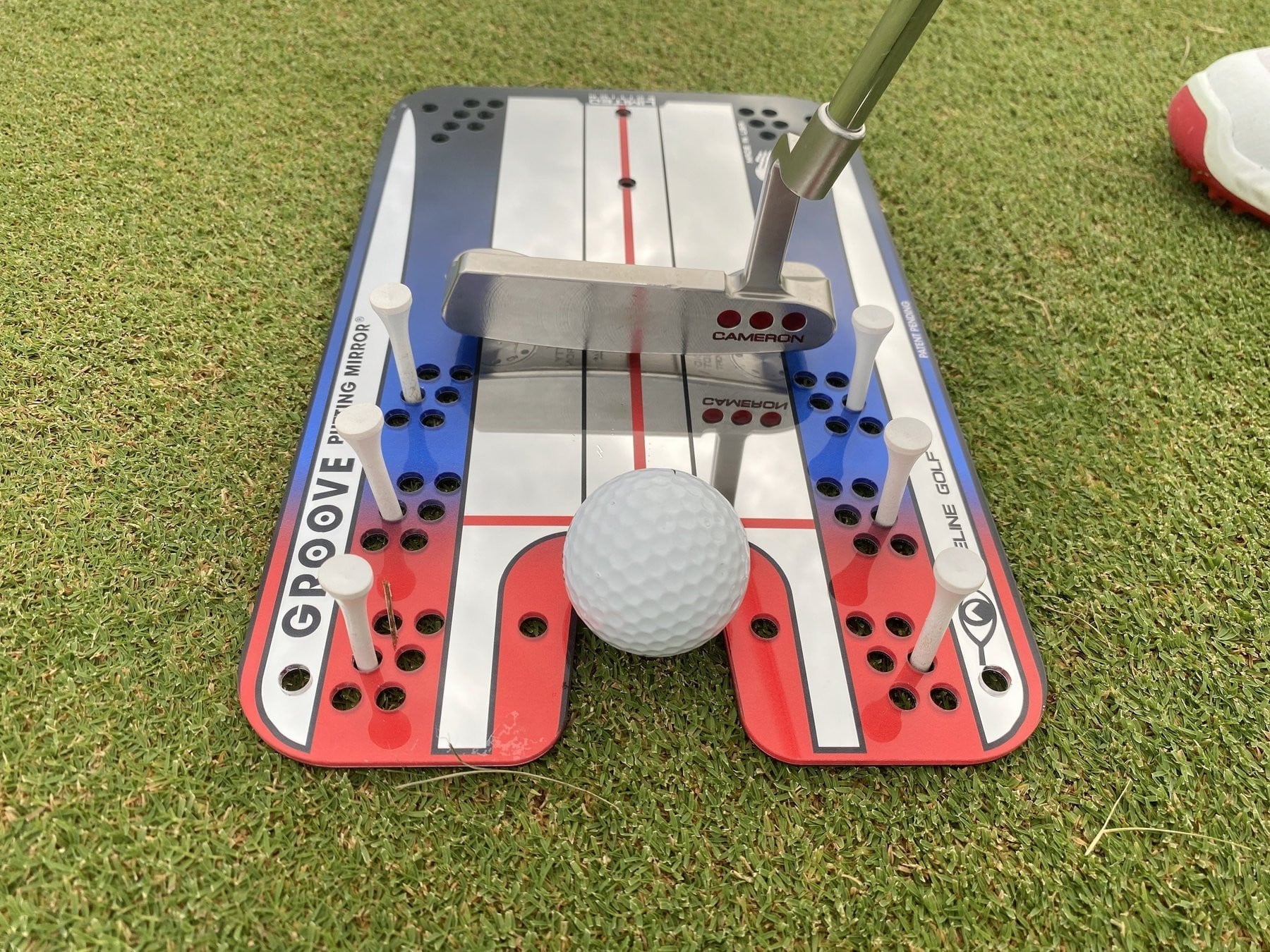 Groove Putting Mirror auf dem Grün, Putter zwischen weißen Gate-Tees, Ball vor dem Spiegel