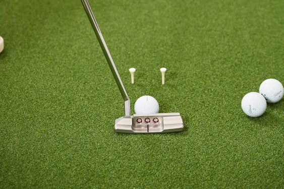 Putter mit Golfball und Tees auf einer Putting-Matte
