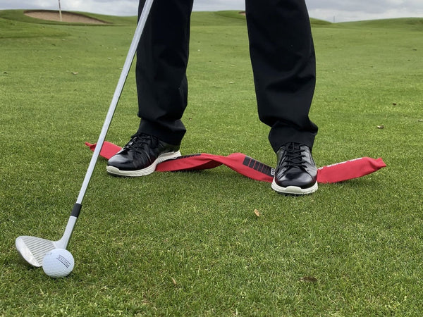 Golfer steht beim Chippen mit beiden Füßen auf dem EyeLine Golf Balance Rod – Balance-Training für konstanten Ballkontakt